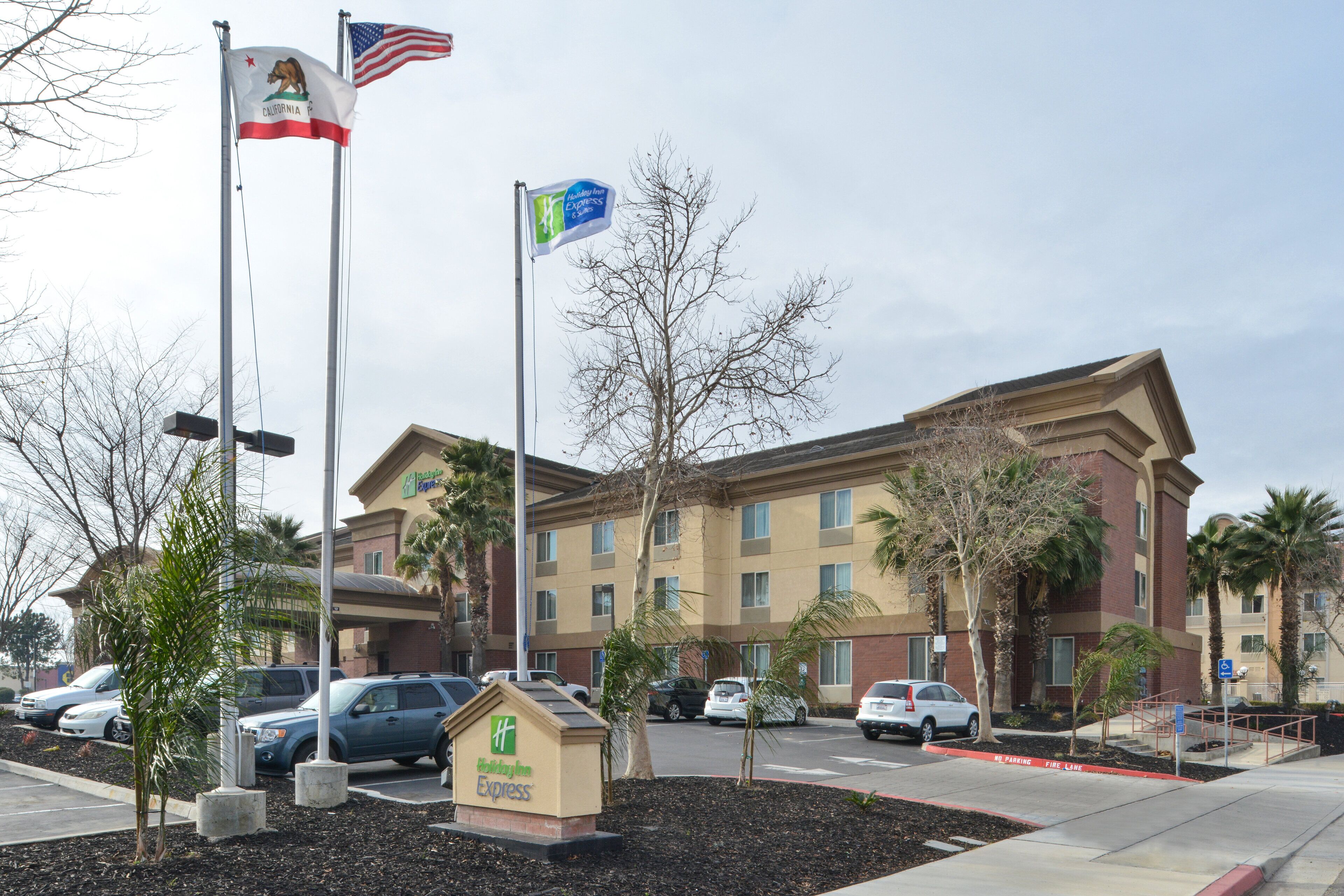 A Holiday Inn Express building with a sign, flags, and parked cars.