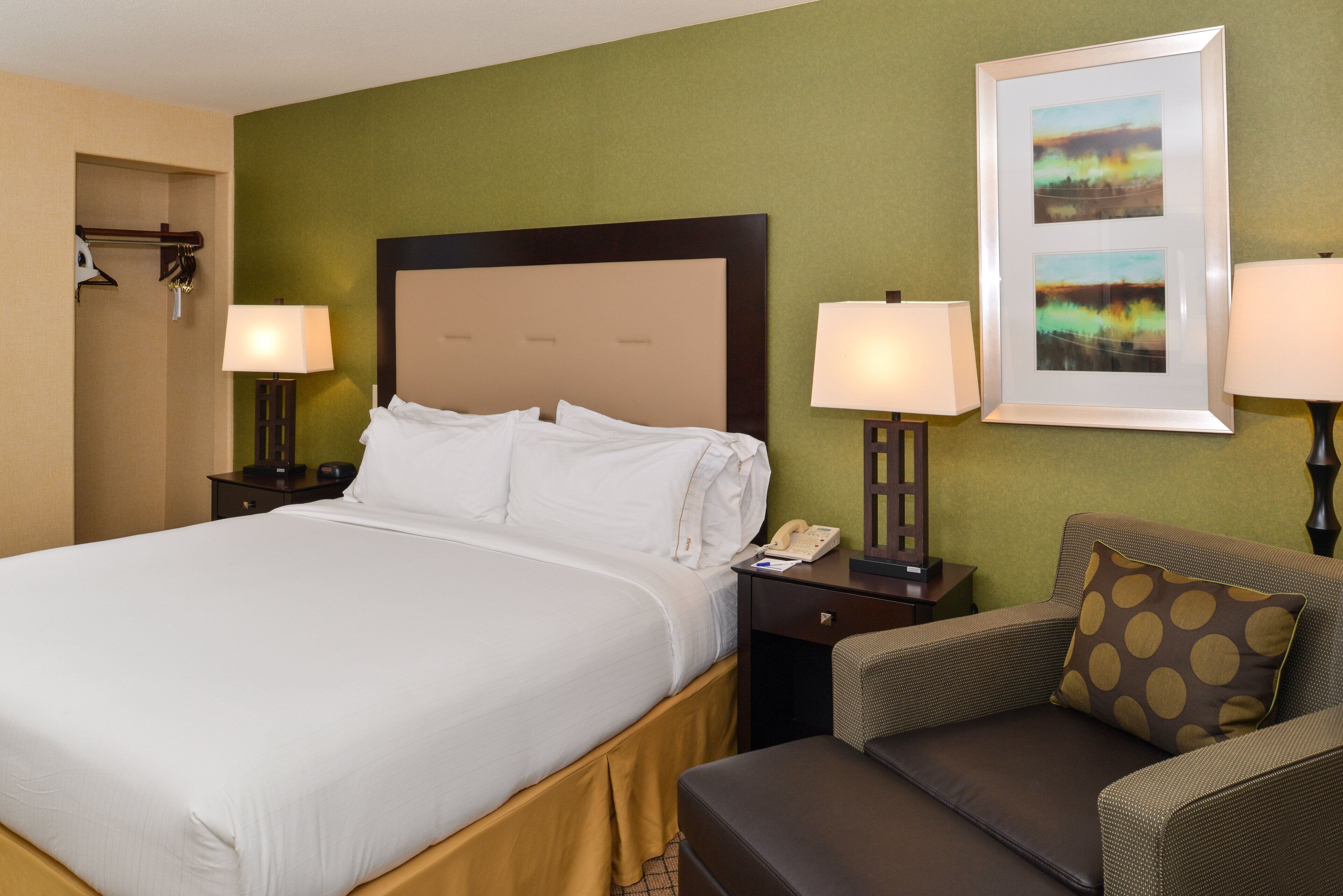 A hotel room with a large bed, two bedside tables with lamps, a chair, and a framed picture on the wall.