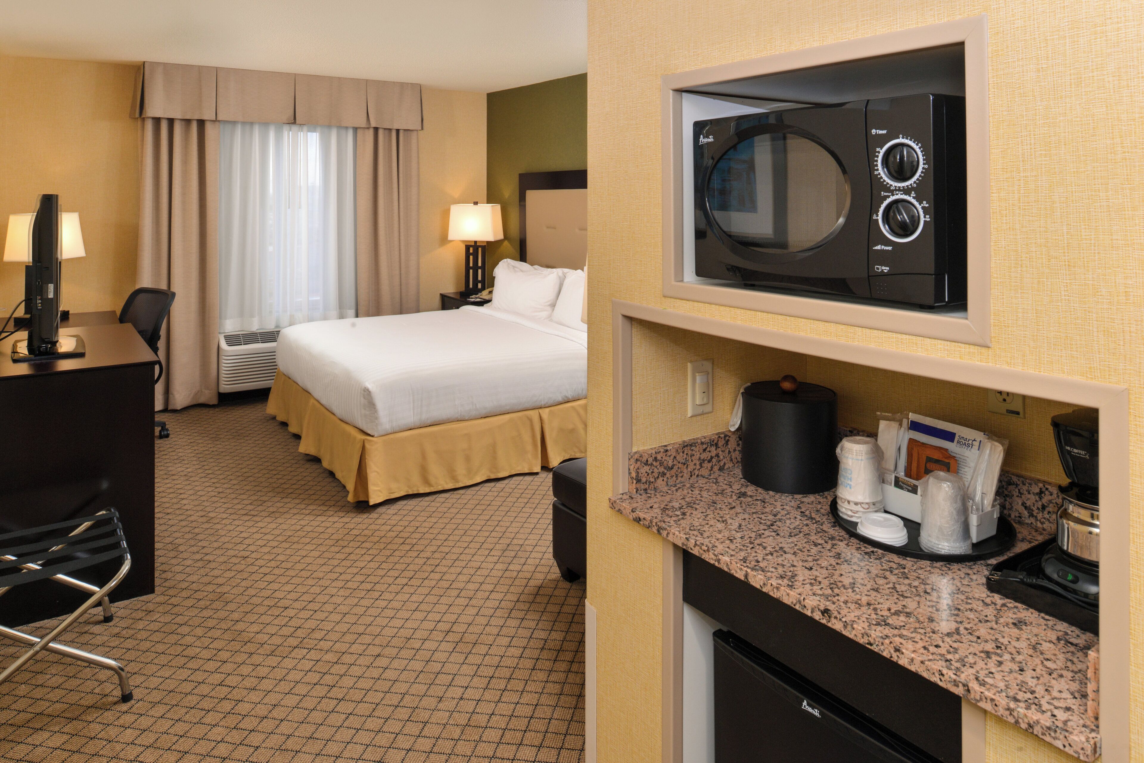 A hotel room with a bed, a desk with a computer, a microwave, and a coffee maker.