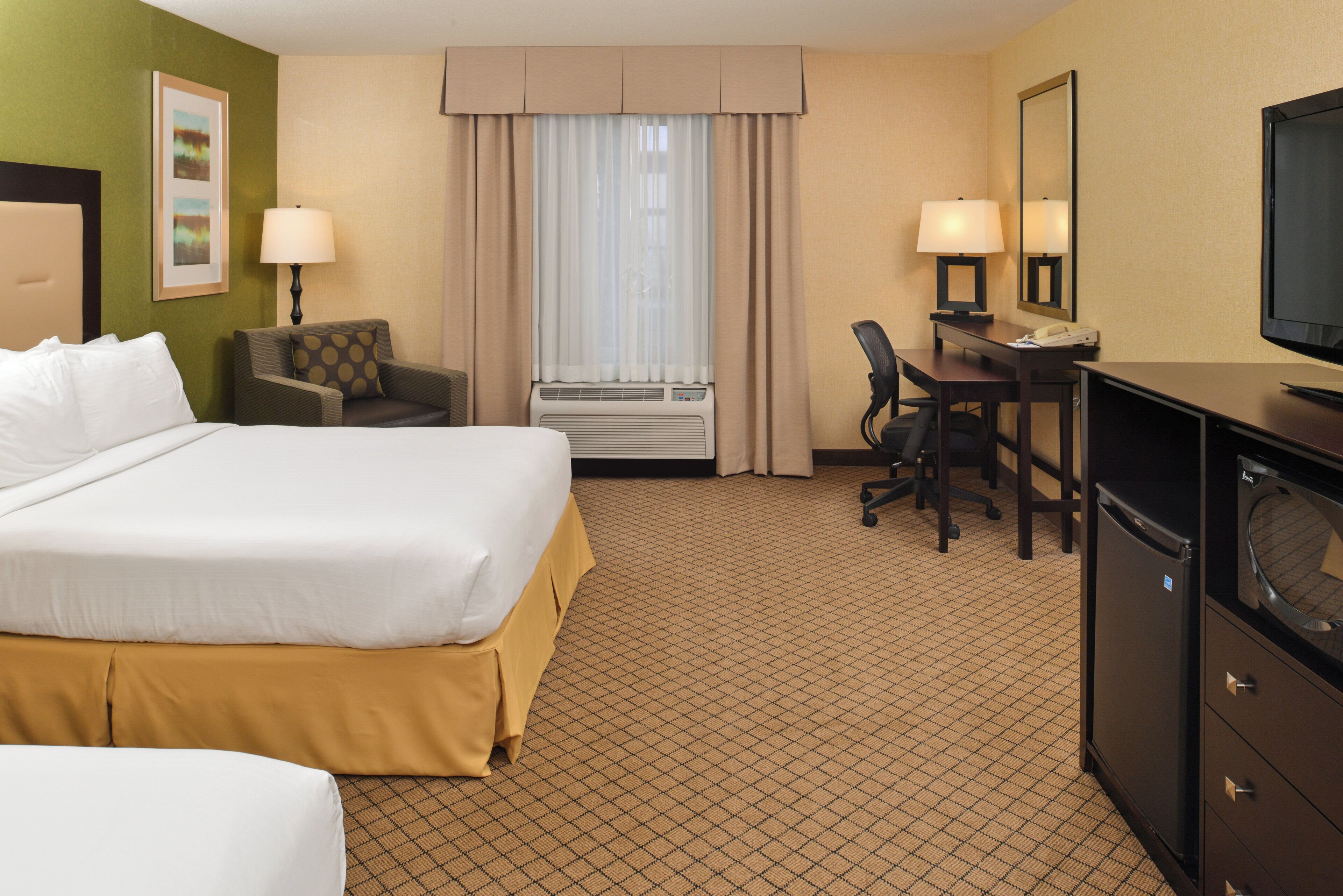 A hotel room with a bed, desk, chair, and a television.