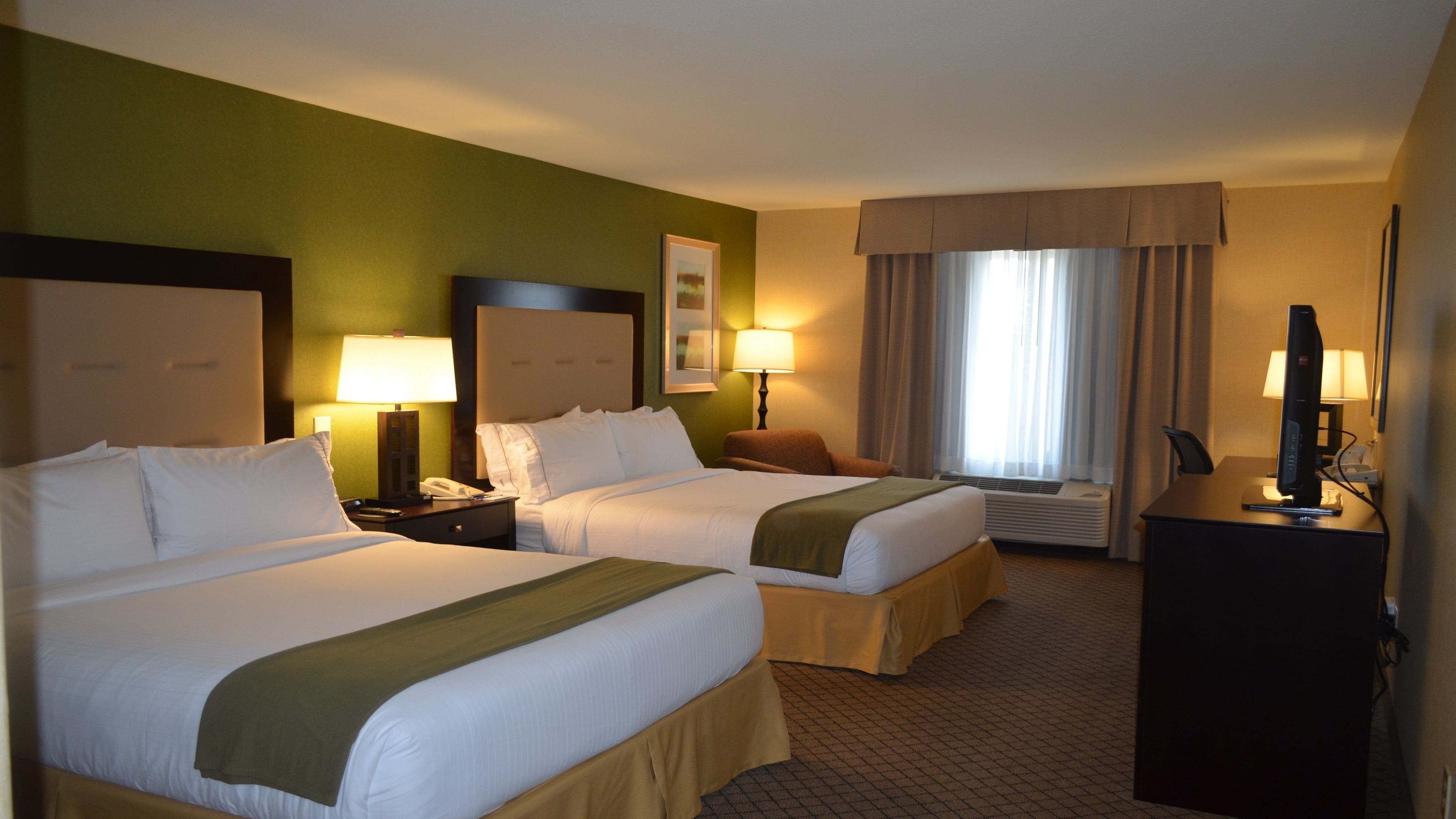 A hotel room with two beds, a desk with a computer, a telephone, and a window with curtains.