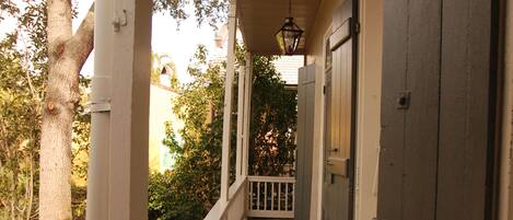 A covered porch with a wooden railing, a view of trees and a building in the background, and a hanging lantern.
