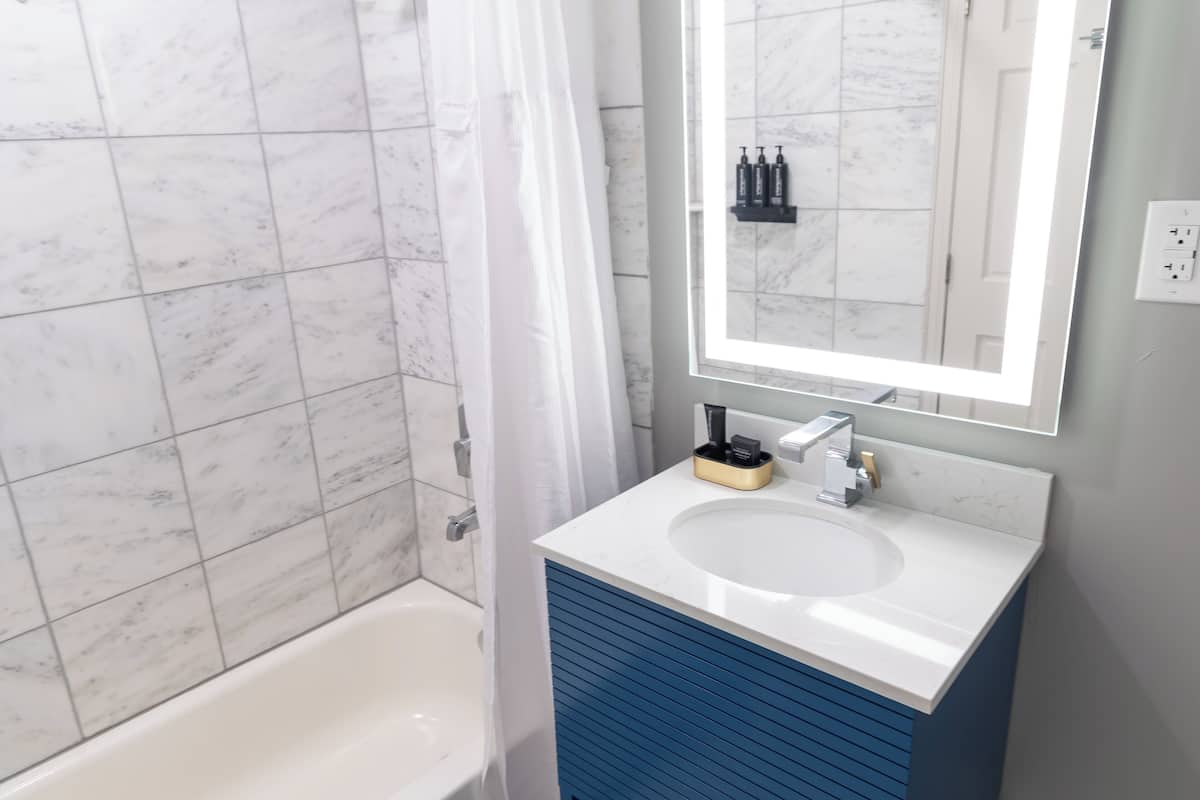 Un baño con una bañera blanca, un lavabo blanco con un mueble azul, y un espejo sobre el lavabo.