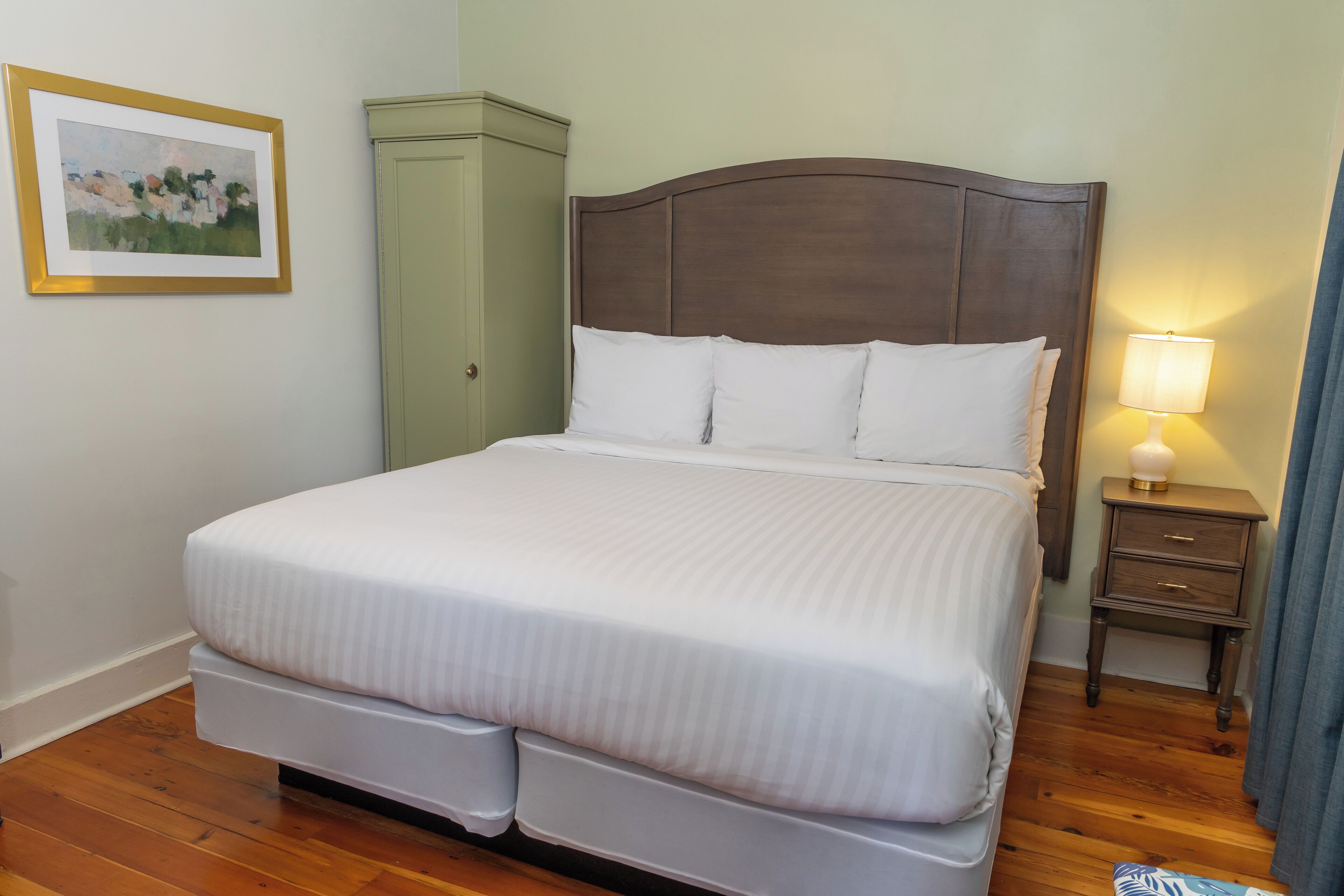 A neatly made bed with a wooden headboard, a bedside table with a lamp, and a green cabinet.