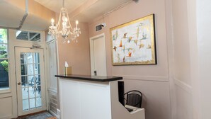 Ein Zimmer mit einem weißen Empfangstresen, einer Kristallleuchtre, einer zur Außenseite führenden Tür und einem Gemälde an der Wand.