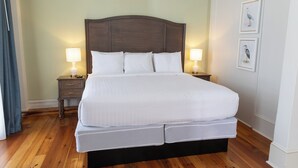 Ein ordentlich bezogenes Bett mit Holz-Kopfteil, zwei Nachttische mit Lampen und gerahmten Wandbildern.