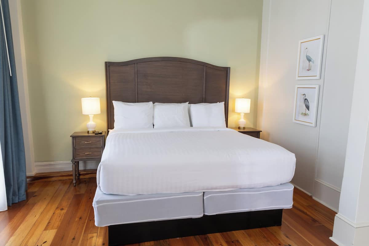 Una cama bien tendida con un cabecero de madera, dos mesitas de noche con lámparas y cuadros en la pared.
