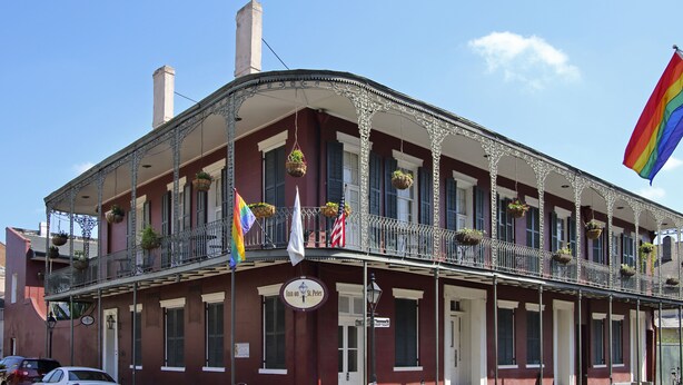 A historic building with a balcony, a sign indicating it is a hotel, and a flag. - Inn on St. Peter (New Orleans)