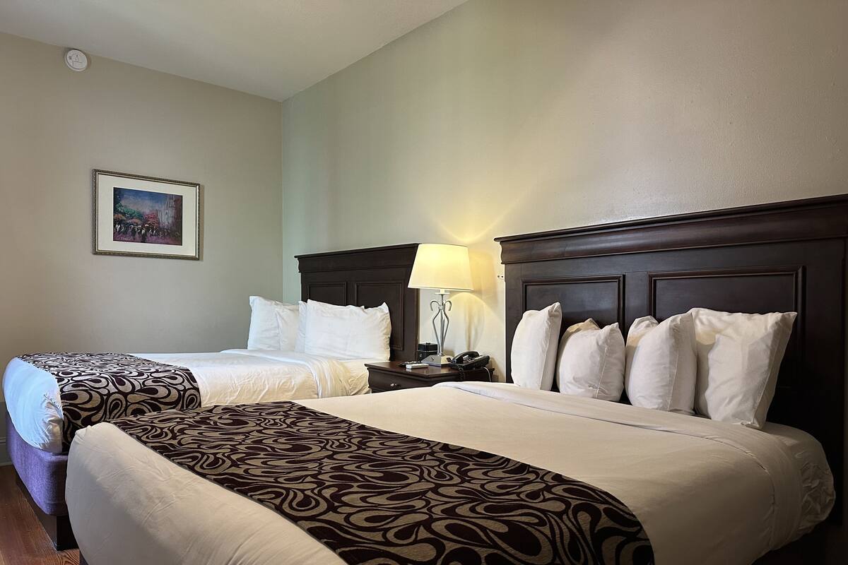 A hotel room with two beds, a nightstand with a lamp, and a framed picture on the wall.