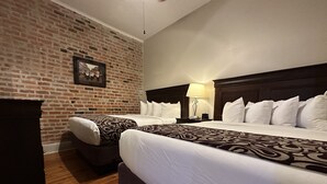 A hotel room with two beds, a brick wall, a wooden floor, and a nightstand with a lamp. - Inn on St. Peter (New Orleans)