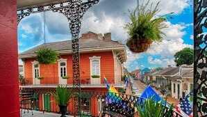 A balcony with a wrought iron railing, a hanging plant, and a view of a street with buildings. - Inn on St. Peter (New Orleans)