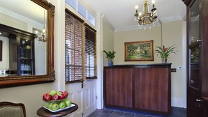 A foyer with a wooden reception desk, a mirror, a chandelier, a painting, and a potted plant. - Inn on St. Peter (New Orleans)