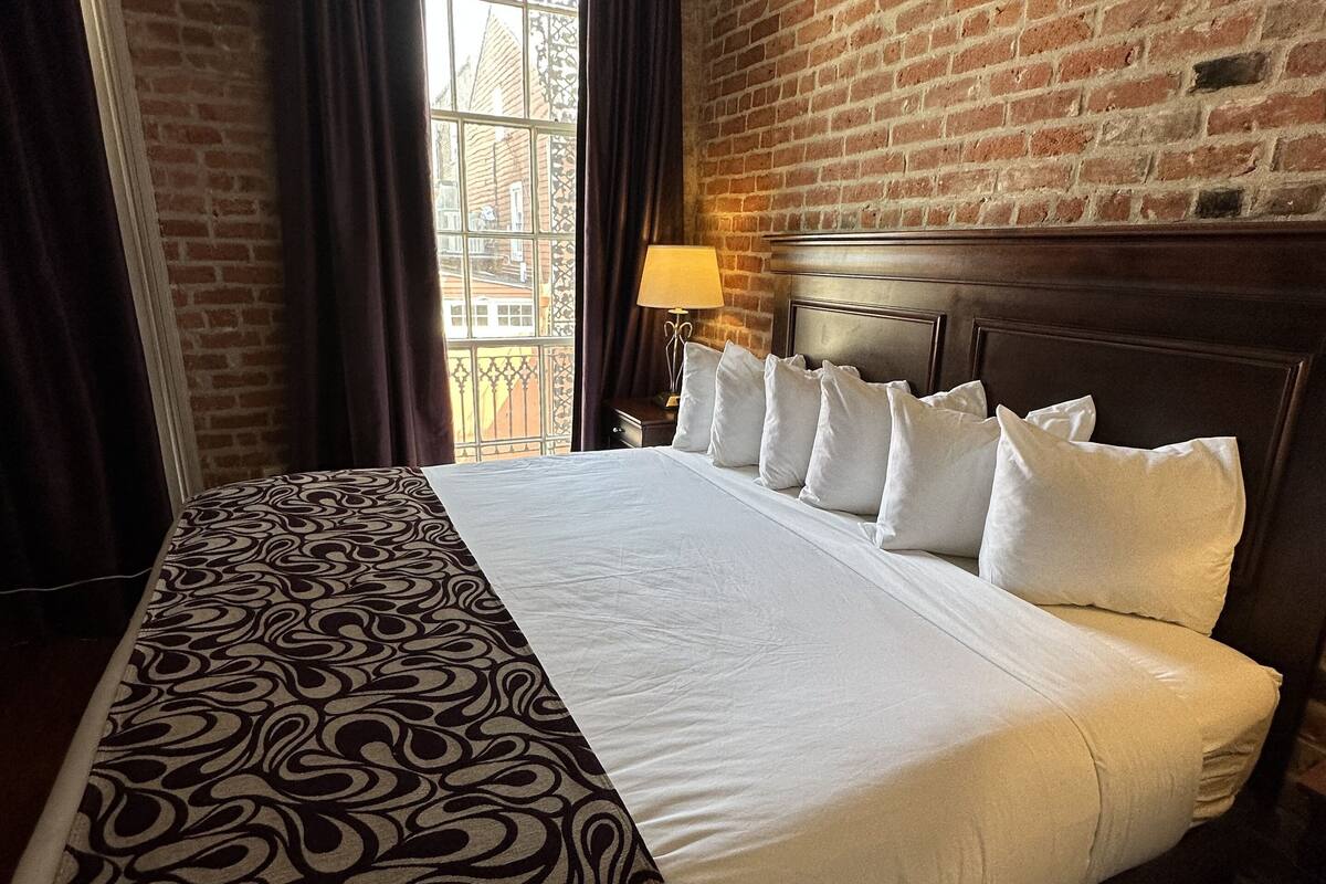 A hotel room with a large bed, a brick wall, and a window with curtains.