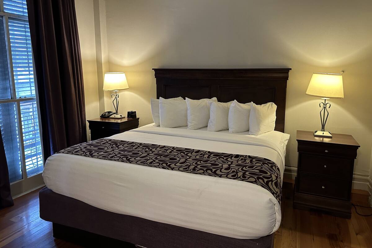 A neatly made bed with a patterned bedspread, two bedside tables with lamps, and a window with curtains.