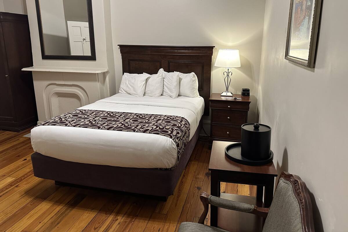 A neatly arranged hotel room with a bed, bedside table, lamp, chair, and a mirror on the wall.