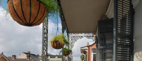 A balcony with hanging planters, a metal railing, and a view of the street below.