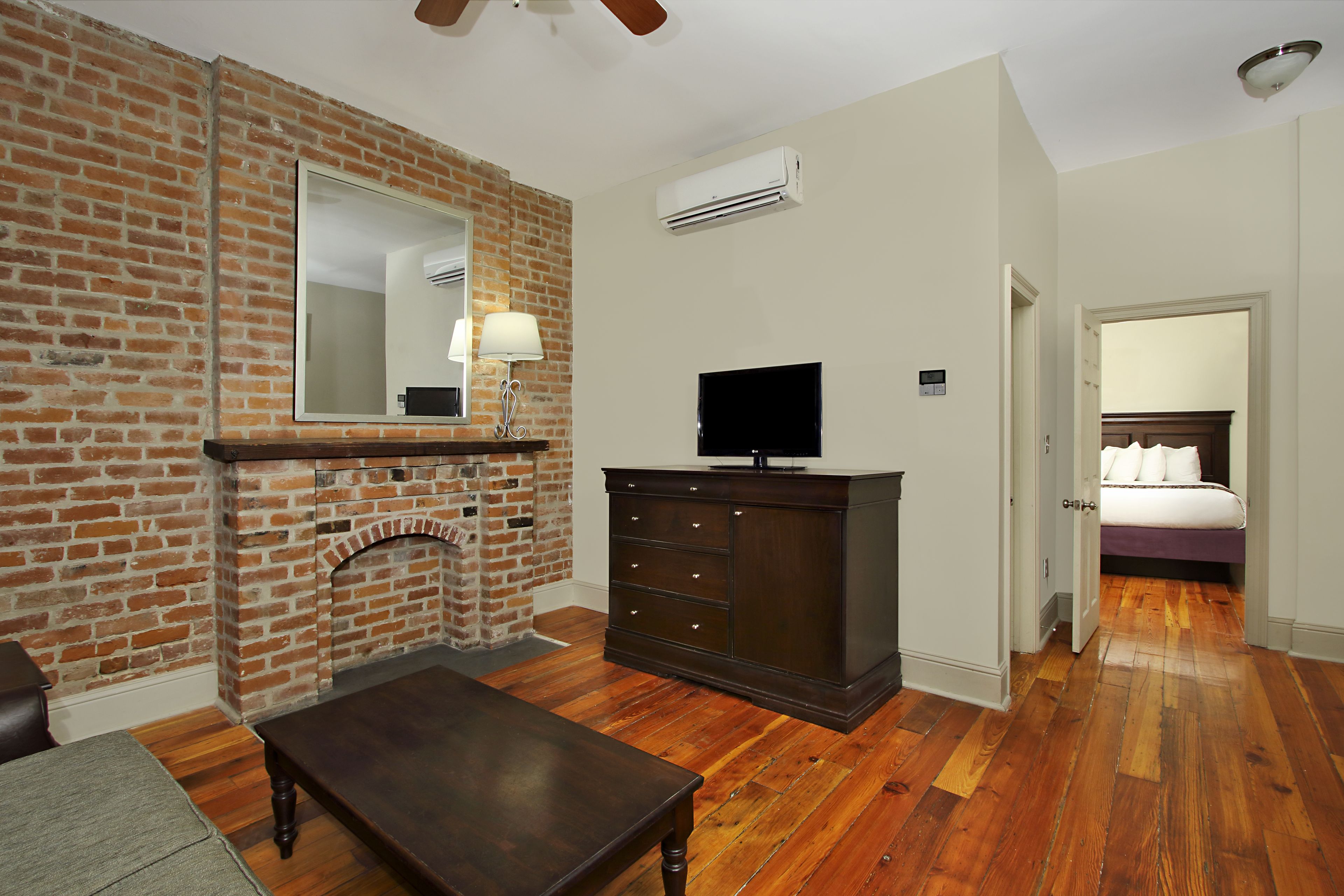 A room with a brick fireplace, a dark wooden cabinet, a television, and a bed in the adjacent room.