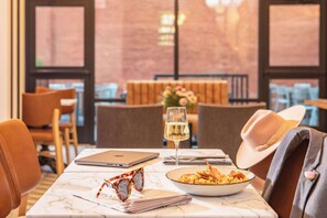 A dining table with a laptop, a wine glass, a plate of food, and a pair of sunglasses.