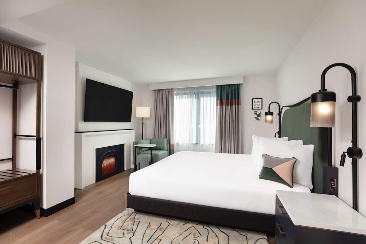 Une chambre d’hôtel avec un lit, un téléviseur fixé au mur, un bureau avec une lampe et une cheminée.