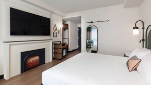 Une chambre d’hôtel moderne dotée d’un grand lit, d’une télévision à écran plat, d’une cheminée, d’une armoire en bois et d’un miroir.
