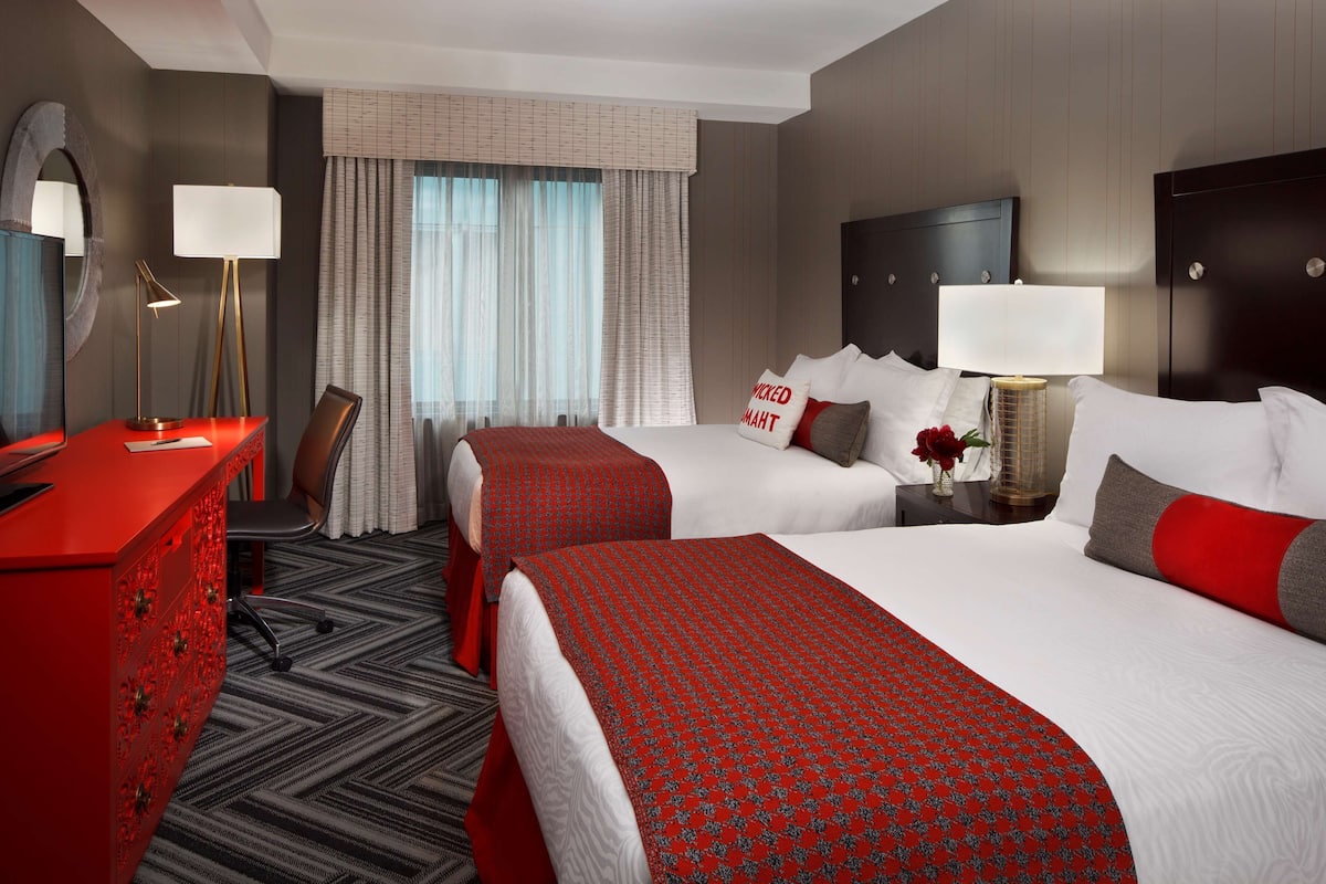 Une chambre d’hôtel avec deux lits, un bureau, une chaise, une commode et une table de chevet avec une lampe.