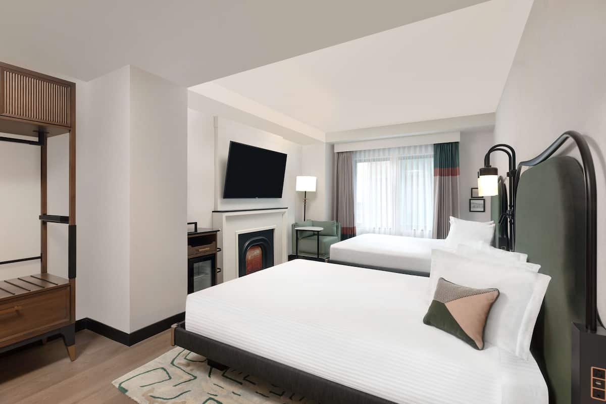 Une chambre d’hôtel avec un grand lit, un téléviseur fixé au mur, un bureau avec une chaise et une cheminée.