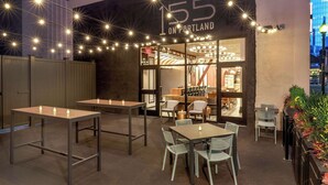 Un restaurant avec des tables et des chaises, une enseigne indiquant « 155, avenue Portland », et une vue sur le paysage urbain en arrière-plan.