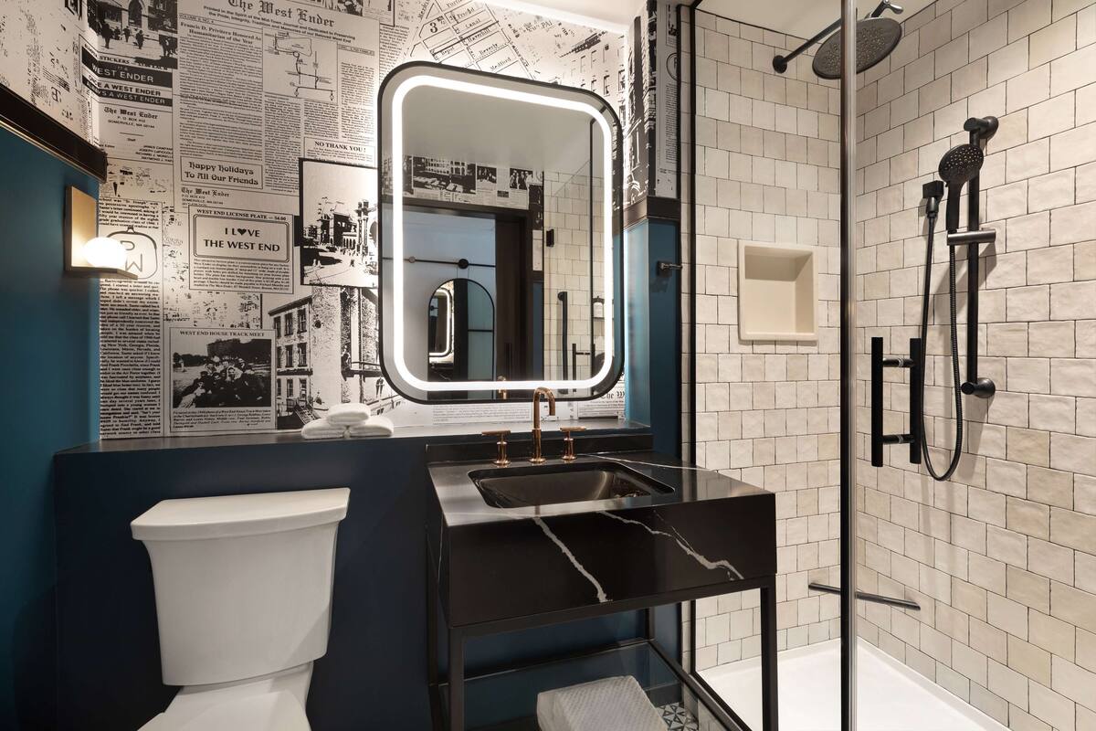 Une salle de bain moderne avec un lavabo noir, des toilettes blanches, une douche en verre et un miroir avec éclairage intégré.
