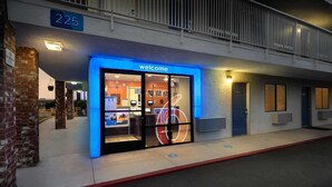 A hotel entrance with a 'Welcome' sign, a number '225' above, and a glass door. - Motel 6 Arcadia, CA - Los Angeles - Pasadena Area (Arcadia)
