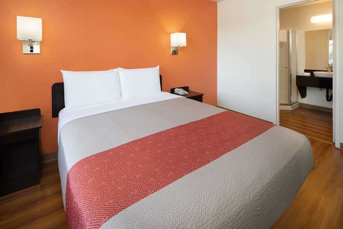 A hotel room with a bed, a nightstand, a telephone, and a bathroom visible through an open door.