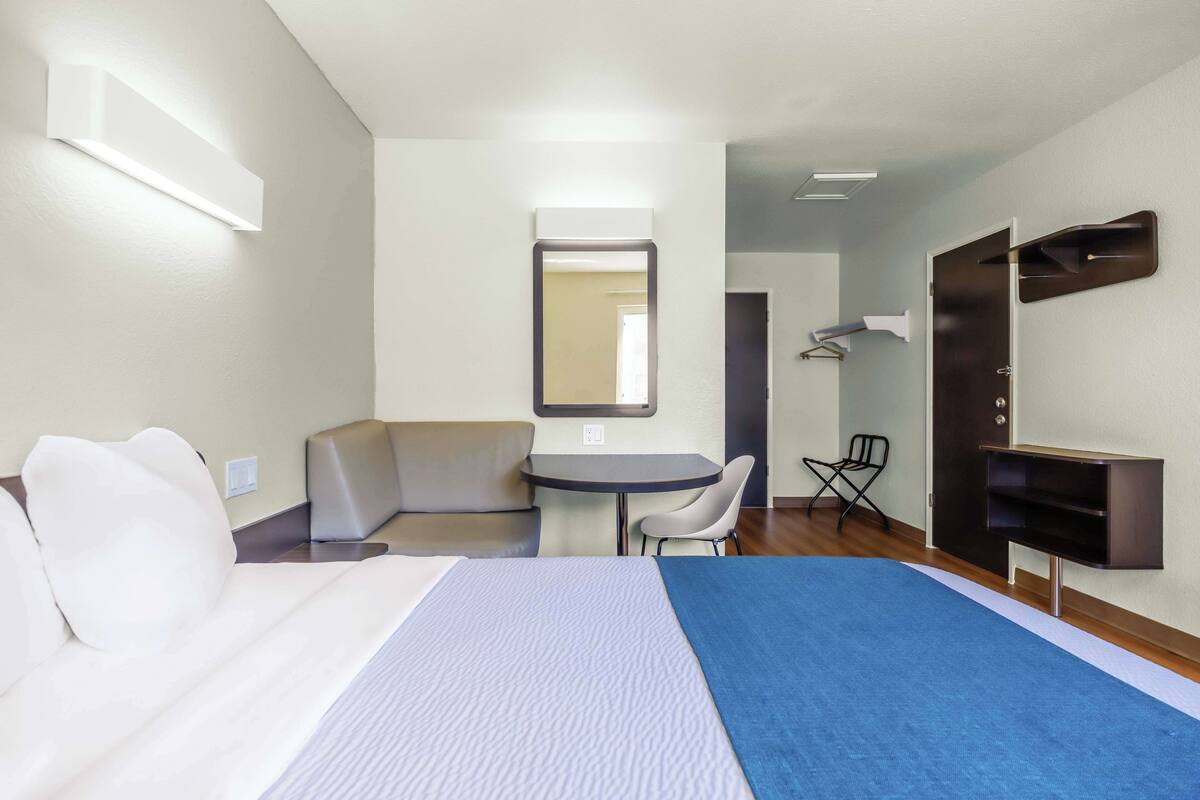 A hotel room with a bed, a desk, a chair, a small table, a mirror, and a wardrobe.