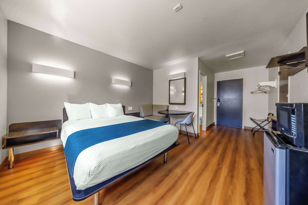 A modern hotel room with a large bed, a desk, a chair, and a TV.