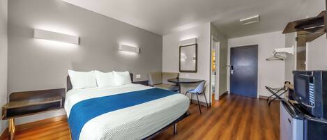 A modern hotel room with a large bed, a desk, a chair, and a TV.