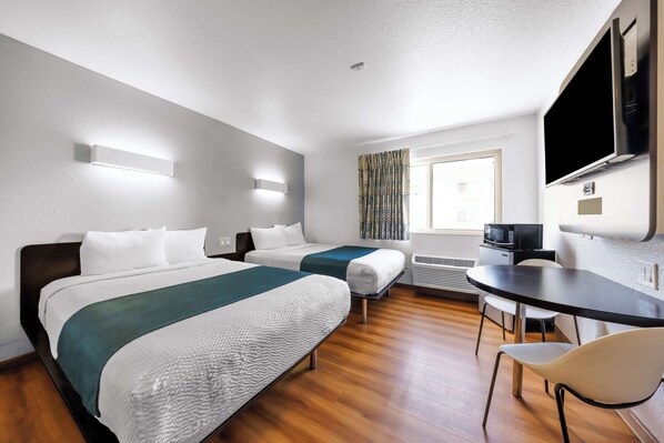 Habitación de hotel con dos camas, un escritorio, una silla, un televisor de pantalla plana y una ventana con cortinas.