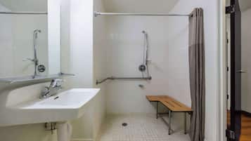 Casa de banho pequena e limpa, com lavatório branco, espelho e chuveiro.