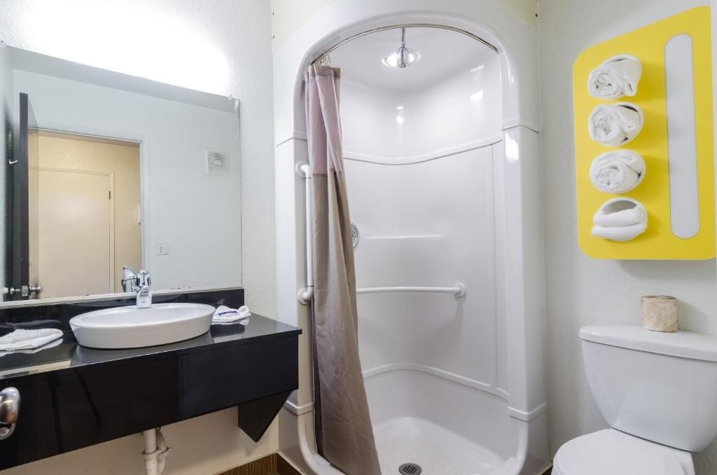 A bathroom with a white sink, a shower with a beige curtain, and a toilet. There is a yellow towel rack with towels.