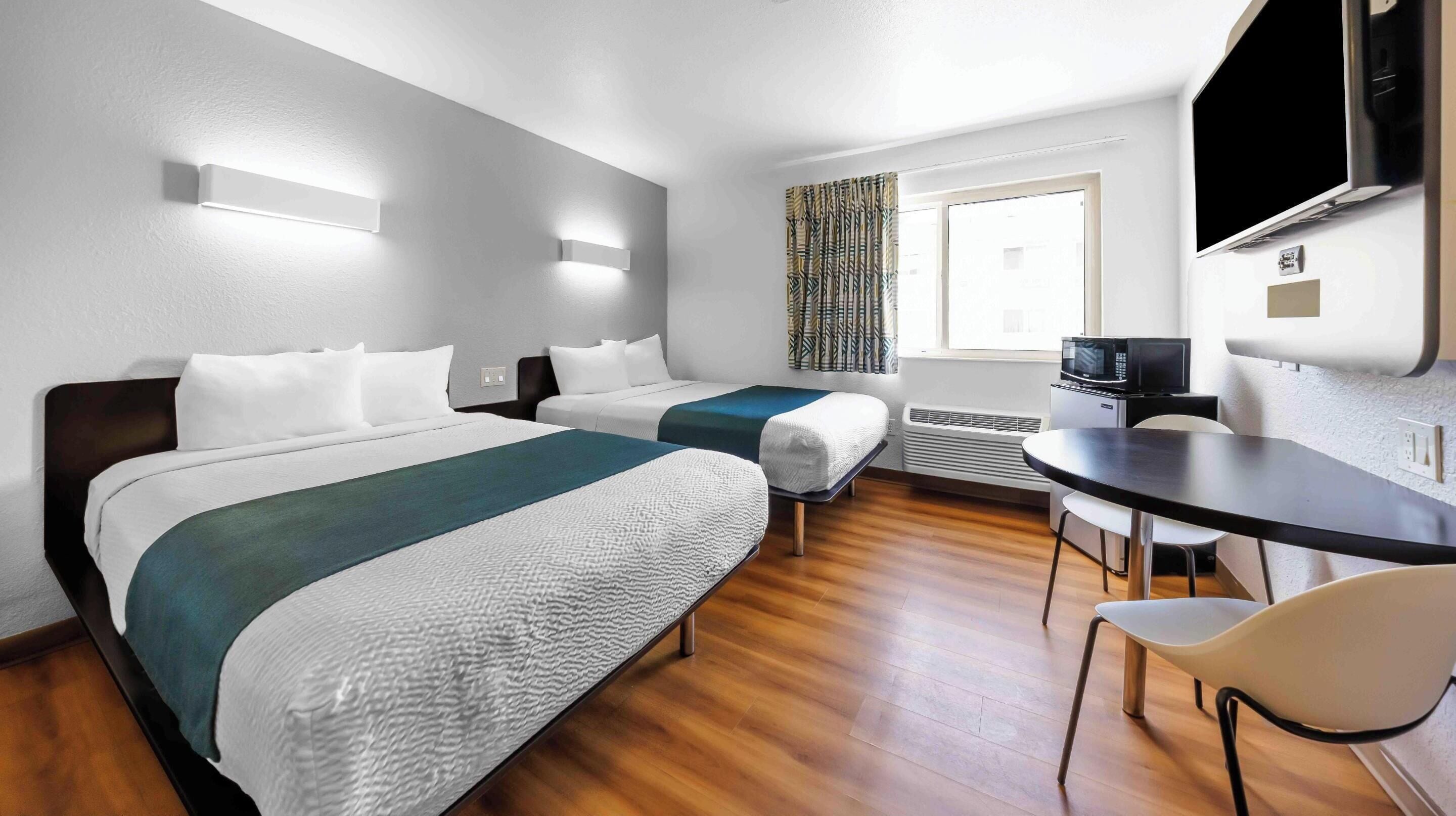 Ein Hotelzimmer mit zwei Betten, einem Schreibtisch, einem Sessel, einem Fernseher und einem Fenster mit Jalousien.