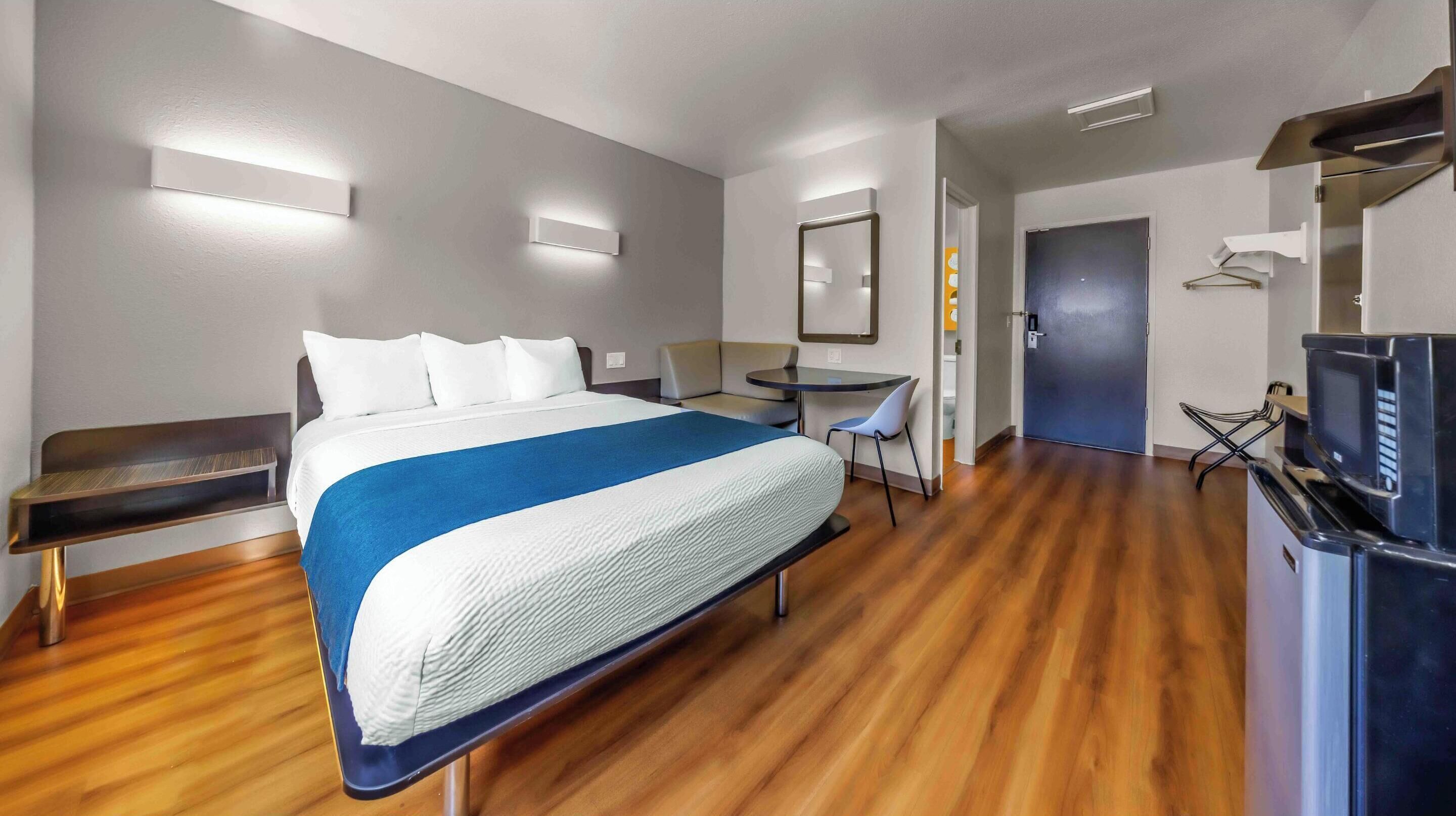 Ein Hotelzimmer mit Bett, Schreibtisch, Stuhl, Fernseher und einer Tür.
