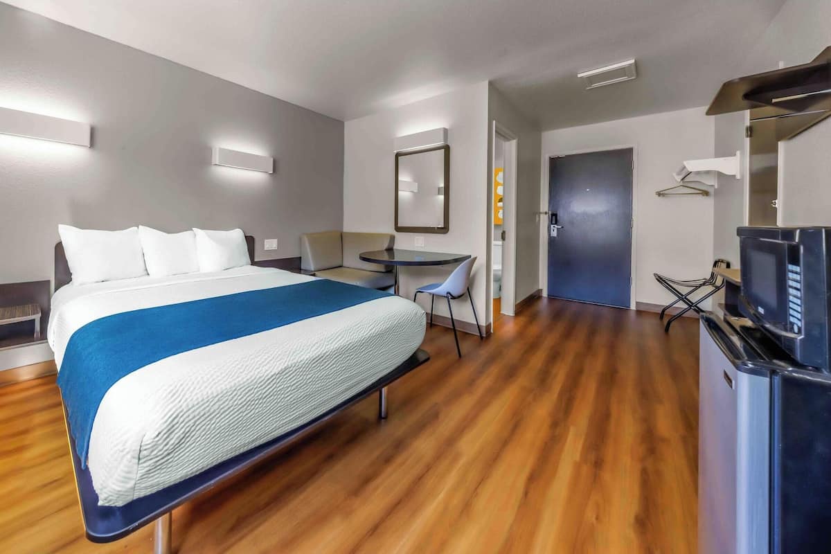 A hotel room with a bed, a desk, a chair, a TV, and a door.