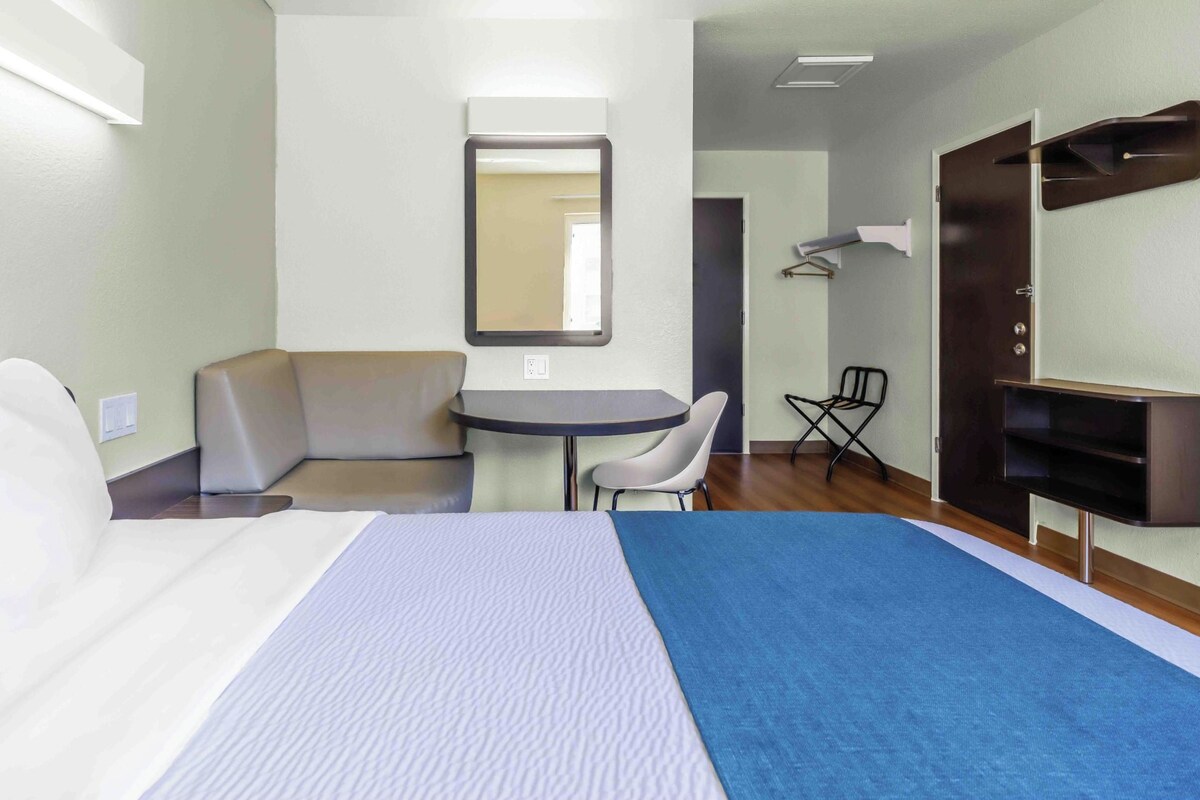 A hotel room with a bed, a desk, a chair, a sofa, a mirror, and a wardrobe.
