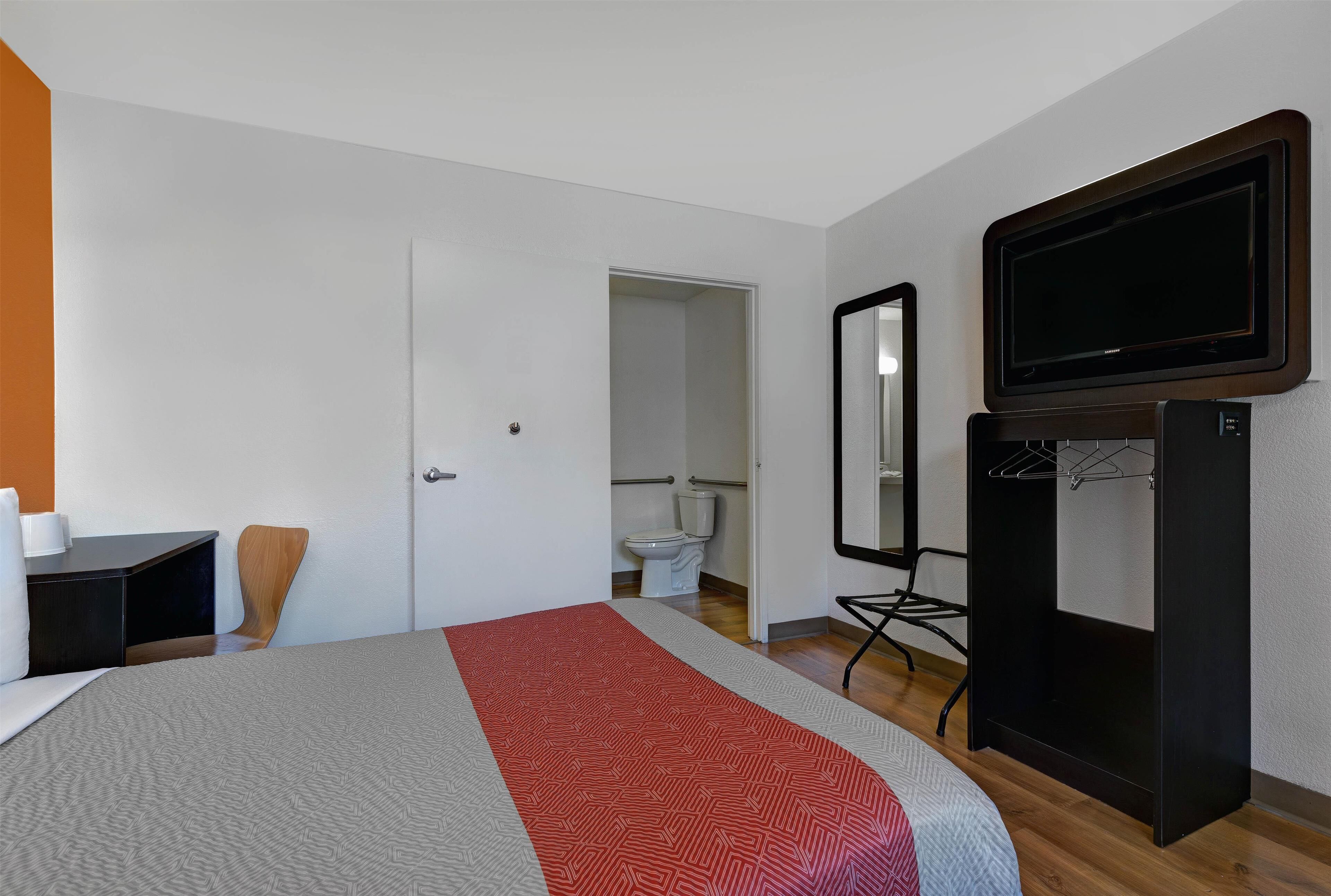 Een hotelkamer met een bed, een bureau, een stoel, een televisie en een spiegel.