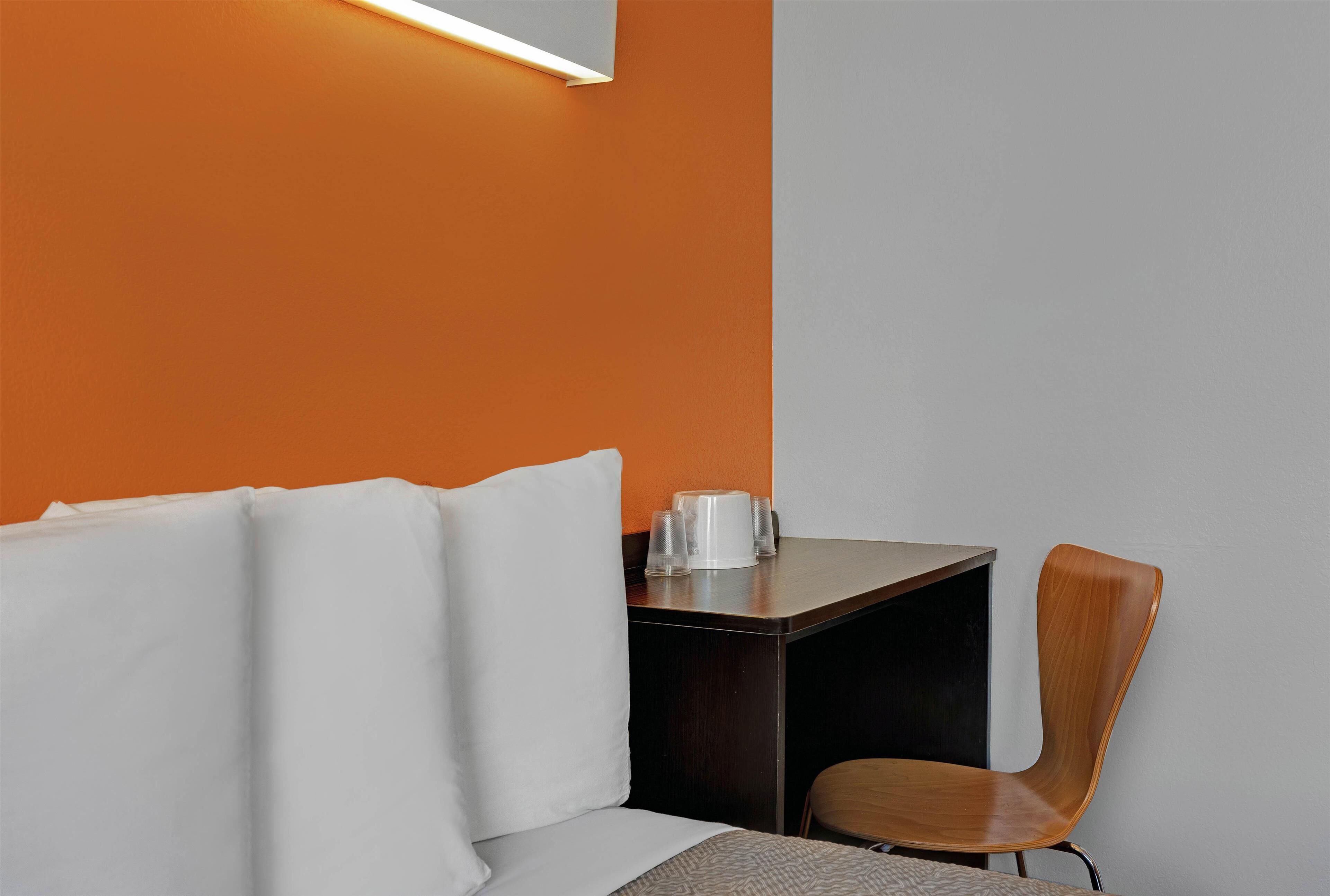 Quarto moderno com sofá branco, cadeira de madeira, pequena mesa com cafeteira e parede em duas cores.