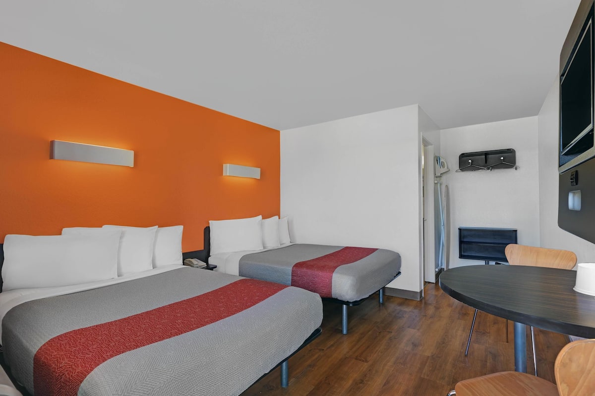 A hotel room with two beds, a dining table, and a TV.