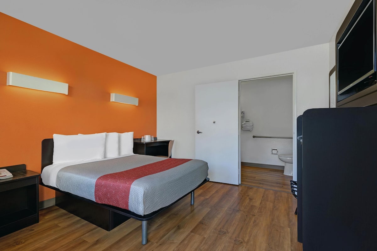 A modern hotel room with a bed, nightstands, a TV, and a bathroom visible through an open door.