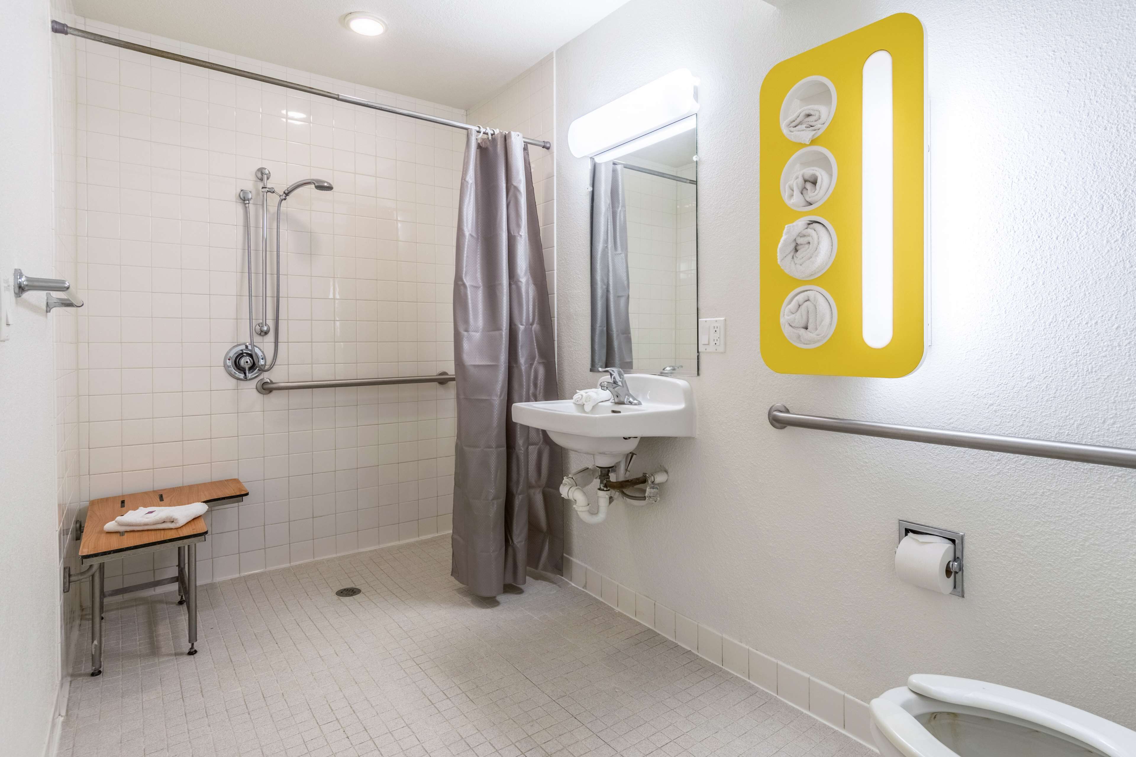 A bathroom with a shower, grab bar, sink, toilet, and a towel rack.