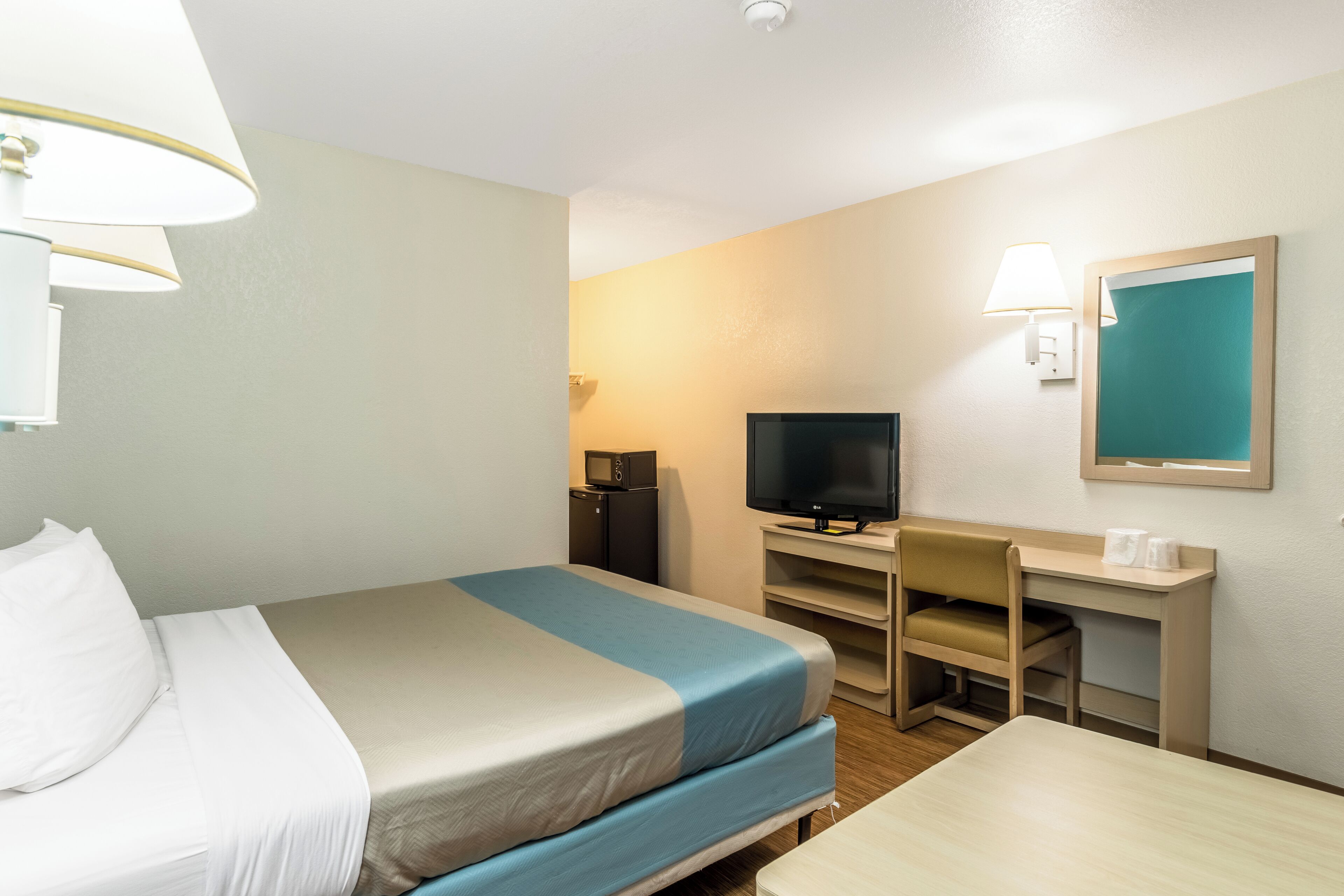 Habitación de hotel con cama, escritorio, televisor y una pequeña kitchenette.