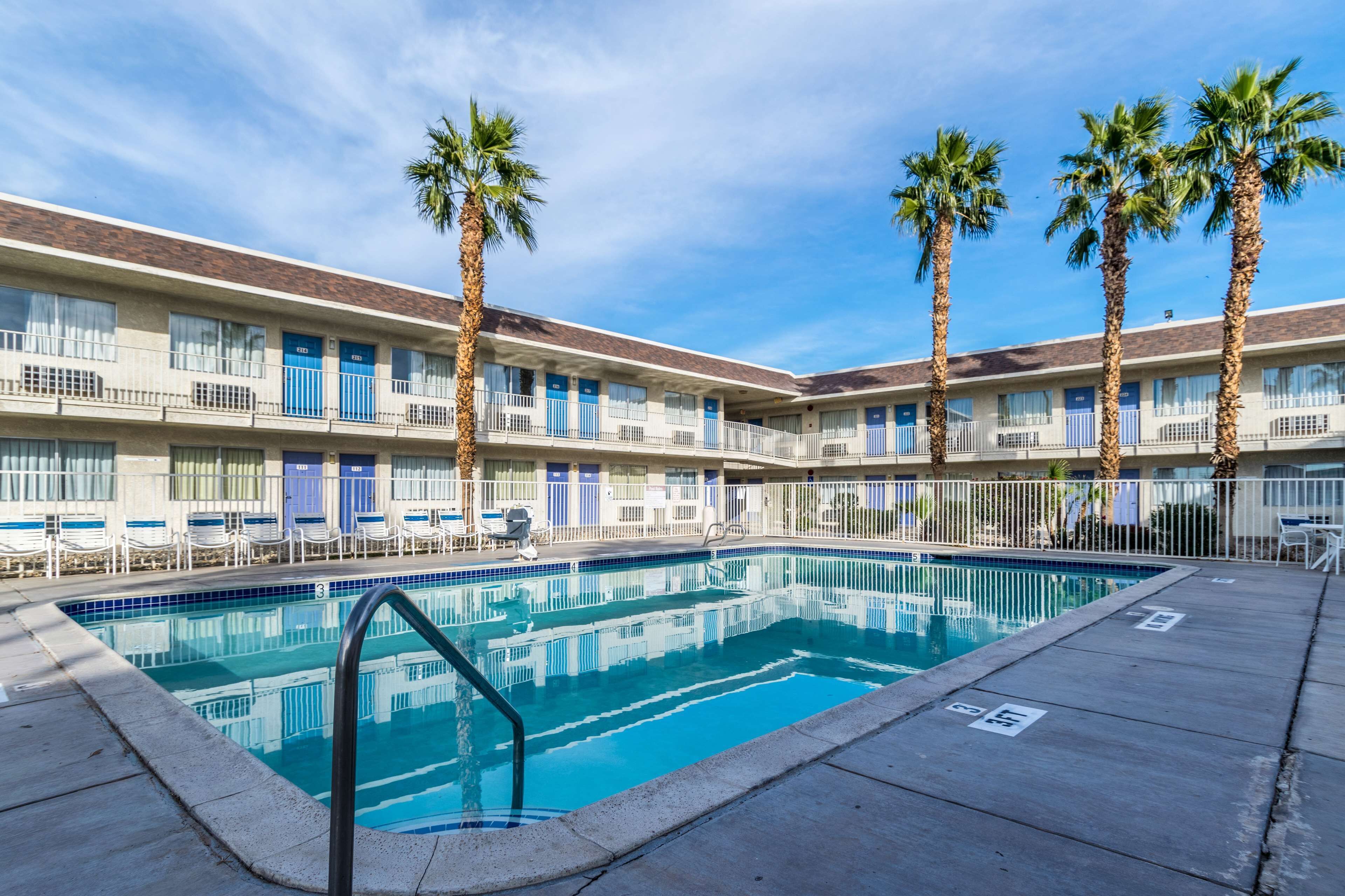 A hotel with a swimming pool, palm trees, and a clear blue sky.