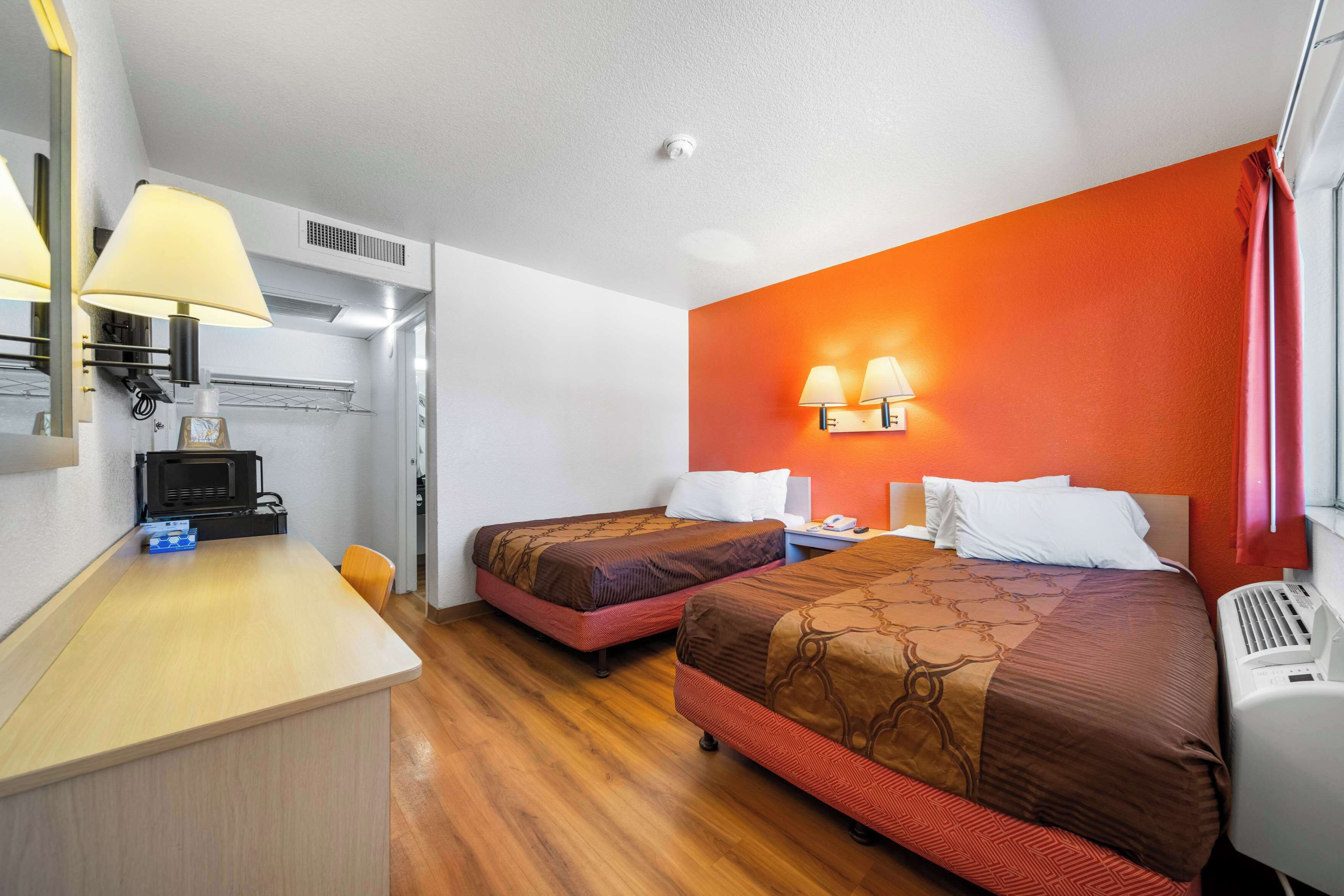 A hotel room with two beds, a desk, a microwave, and a small kitchenette.