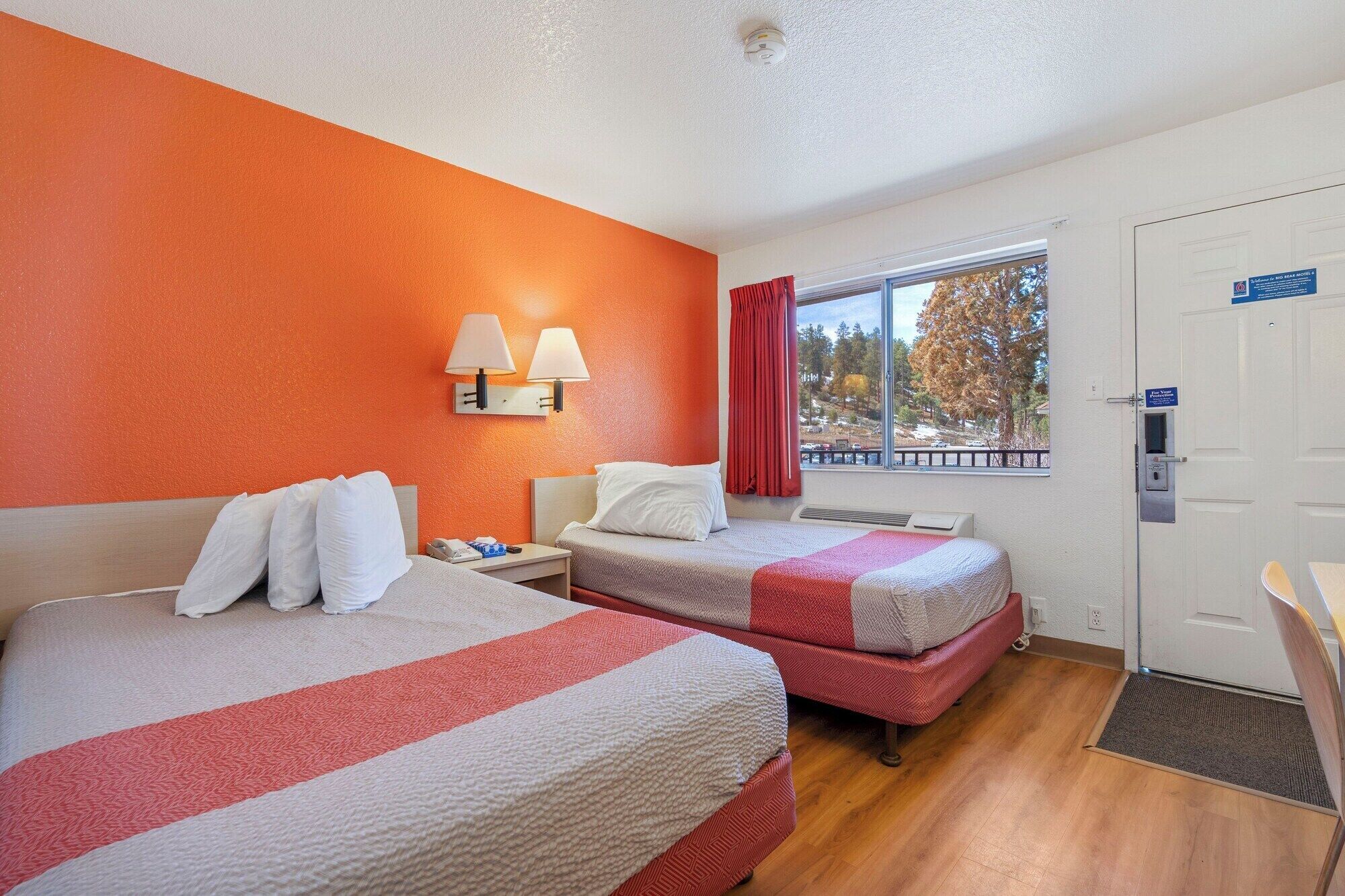 Une chambre d’hôtel avec deux lits, une fenêtre donnant sur un paysage agréable, une porte avec une pancarte et un mur muni d’un luminaire.