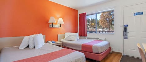 A hotel room with two beds, a window with a view, a door with a sign, and a wall with a light fixture.